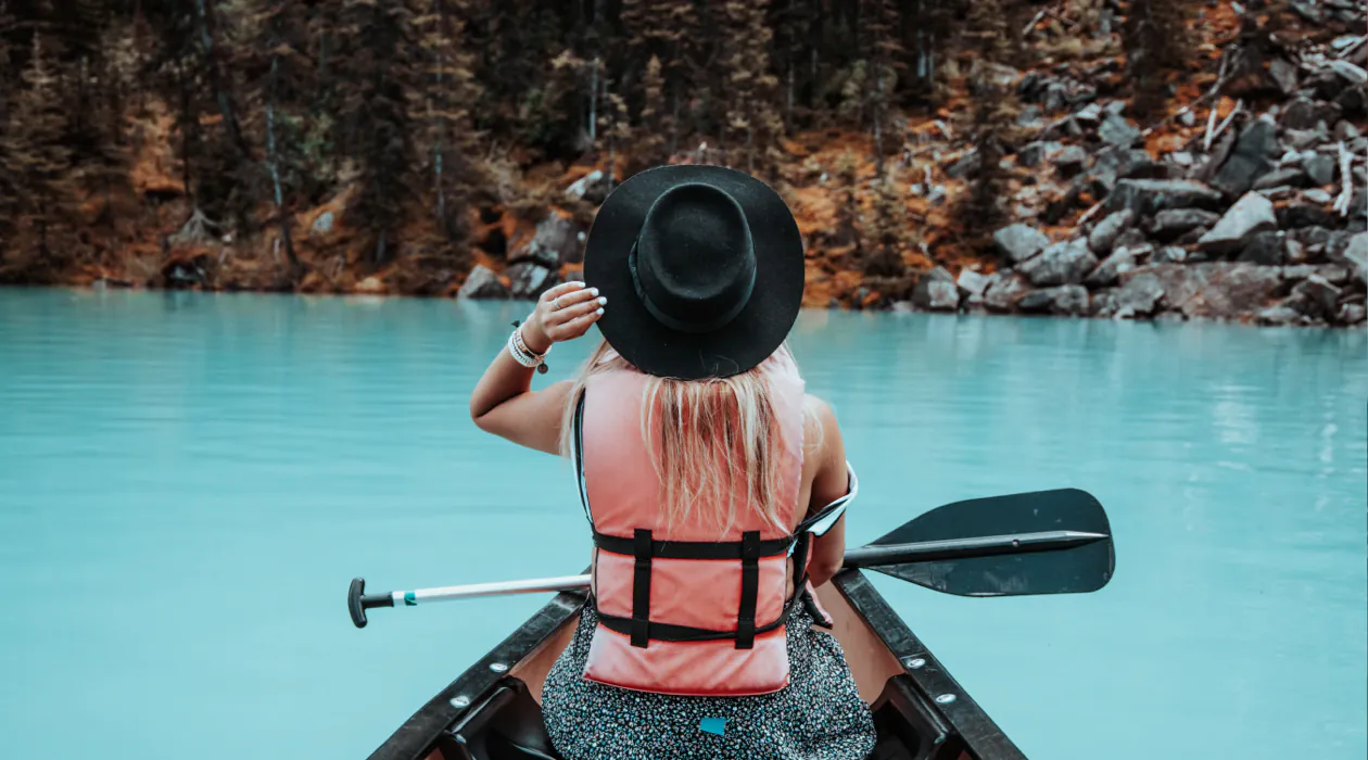 woman kayaking in turquoise water with a hat on.