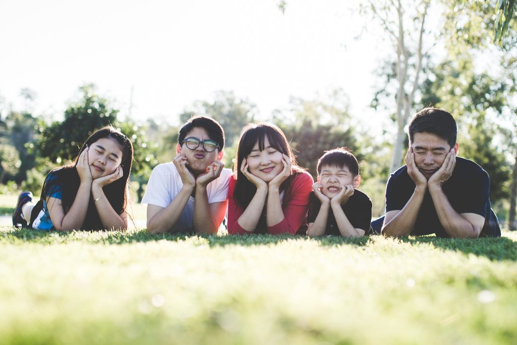 Smiling family of five laying on grass while propping their heads in their hands.