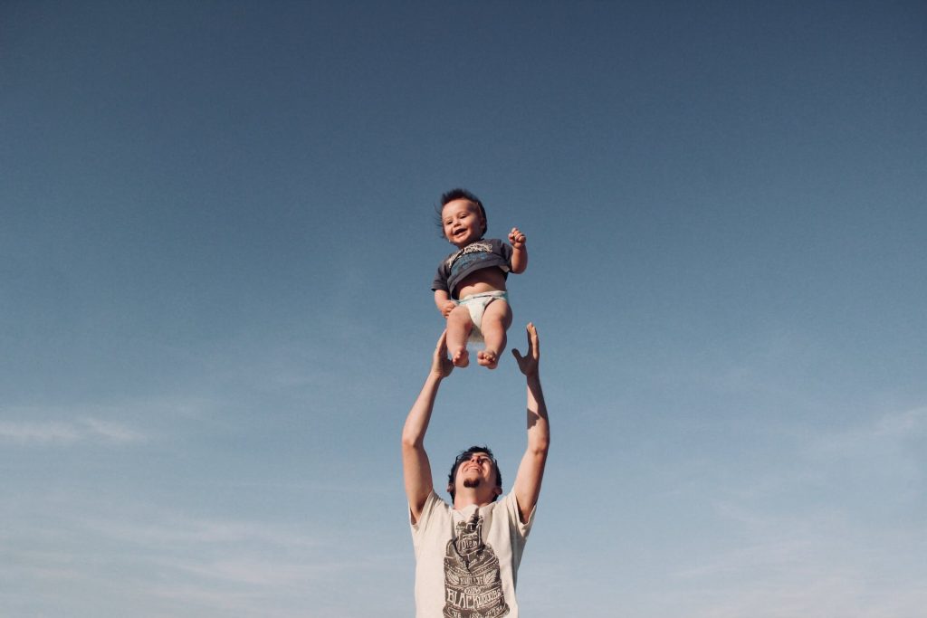 A father tossing baby up into the air with a blue sky in the background.