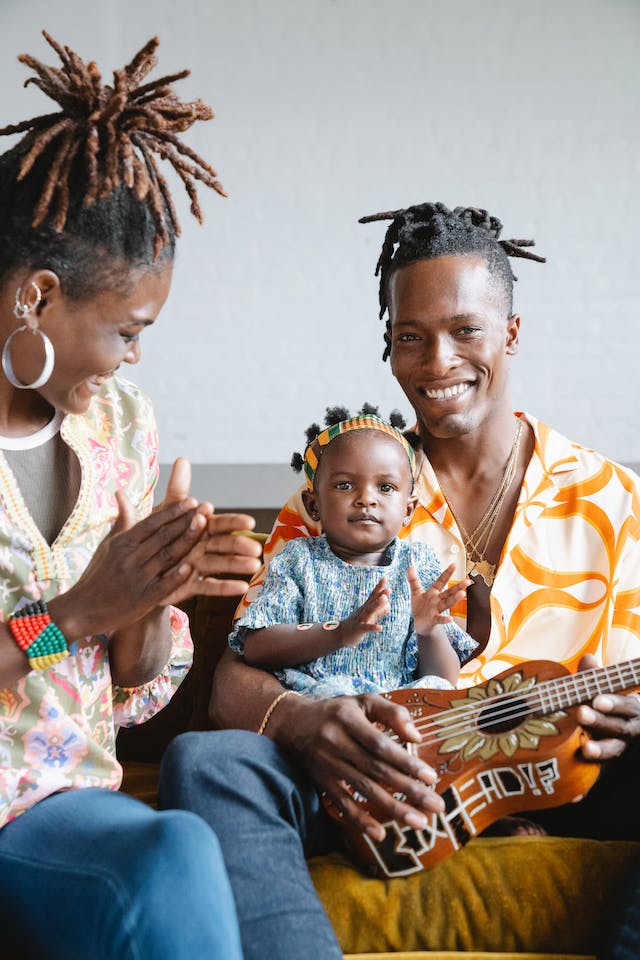 Father of three playing music with a guitar and dressed in traditional African colors and jewelry.