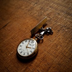 Gold pocket watch with a button hole peg on the end of the chain for fastening to a jacket or pants.