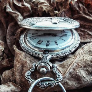 Engraved silver pocket watch lying on fall foliage
