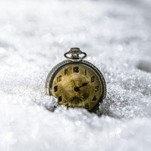 An antique silver watch with faded face details and a seconds keeping subdial sits dramatically against freshly fallen snow.