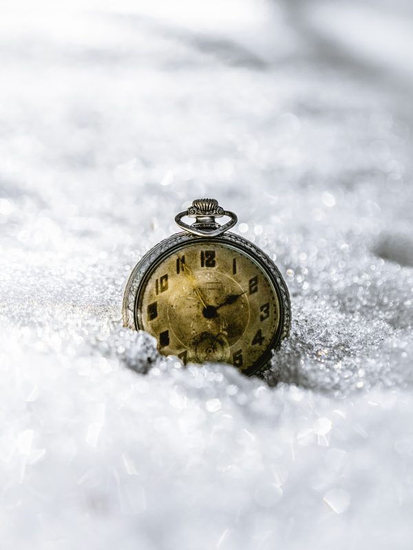 An antique silver watch with faded face details and a seconds keeping subdial sits dramatically against freshly fallen snow.