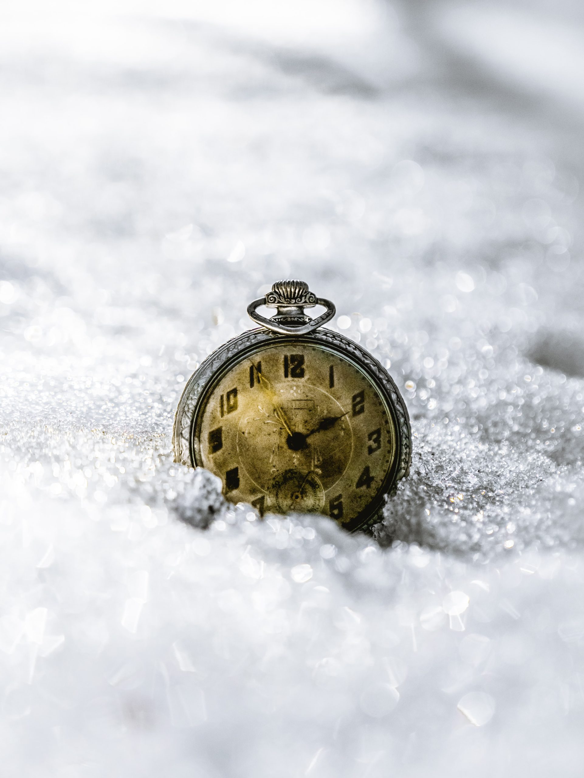 An antique silver watch with faded face details and a seconds keeping subdial sits dramatically against freshly fallen snow.