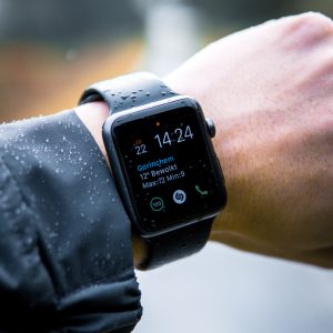 A mans wrist wearing a smart watch with a black band.