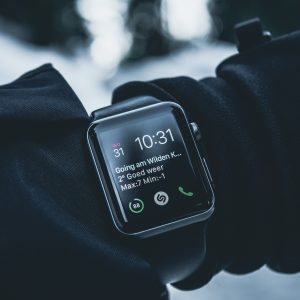 Black cased smart watch with a black band on an arm wearing a black coat in the winter time.