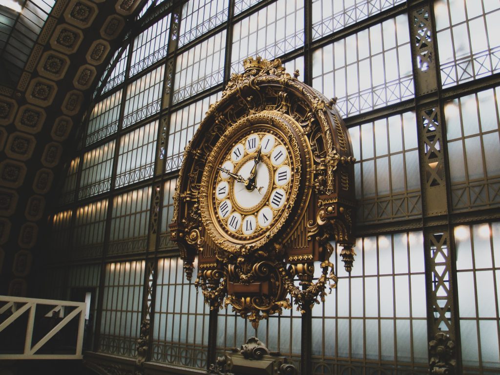 Giant golden clock with intricate carvings hanging in a train station.