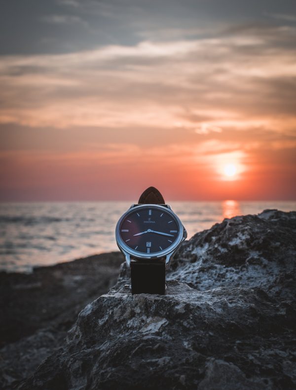 T watch by Festina sitting on a rock near the shore with the ocean and a sunset in the background.